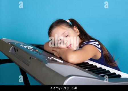 Nahaufnahme eines schlafenden Mädchens auf den Tasten eines elektronischen Synthesizers, müde in der Musikschule, isoliert auf blauem Hintergrund Stockfoto