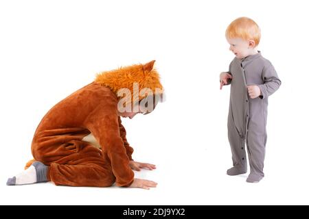 Auf weißem Hintergrund spielt das Kind mit seinem Bruder, gekleidet in ein Karnevalslöwenkostüm. Älterer und jüngerer Bruder spielen. Lustige Kinder. Stockfoto