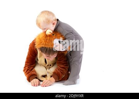 Auf weißem Hintergrund spielt das Kind mit seinem Bruder, gekleidet in ein Karnevalslöwenkostüm. Älterer und jüngerer Bruder spielen. Lustige Kinder. Stockfoto