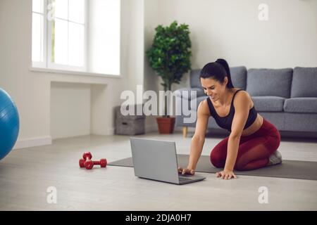 Frau, die zu Hause auf einer Sportmatte sitzt, online Sportkleidung kauft oder sich eine Video-Trainingsstunde anschaut Stockfoto