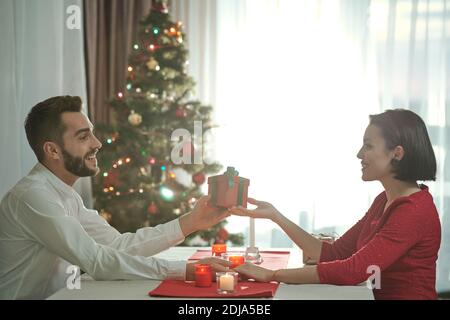 Glücklich schöne junge Paar sitzt am Tisch mit brennenden Kerzen Und Hände halten, während Sie Weihnachtsgeschenke austauschen Stockfoto