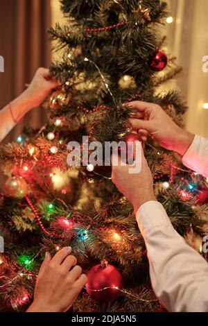 Nahaufnahme eines nicht erkennbaren Mannes, der während der Weihnachtskugel am Baum hängt Weibliche Hände einstellen Weihnachtsbeleuchtung Stockfoto