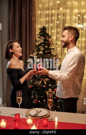 Lächelnd anhänglich junger Mann mit Bart geben Weihnachtsgeschenk zu Aufgeregt Freundin am Weihnachtsabend Stockfoto
