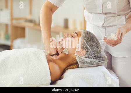 Kosmetikerin deckt junge Frauen Gesicht mit feuchtigkeitsspendenden Maske oder Creme Nach der Hautpflege Verfahren Stockfoto