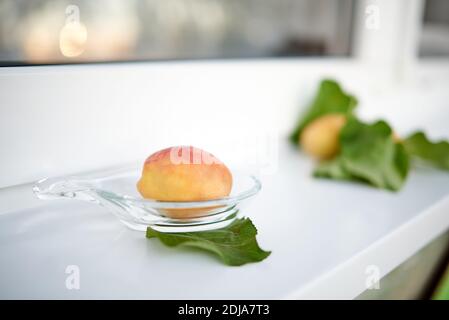 Aprikosen und ihre Blätter liegen auf einer weißen Fensterbank. Selektiver Fokus Stockfoto