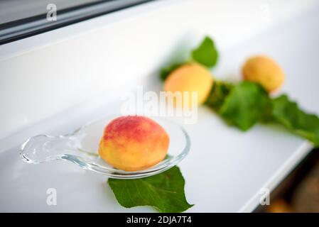 Aprikosen und ihre Blätter liegen auf einer weißen Fensterbank. Selektiver Fokus Stockfoto