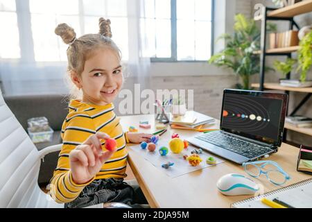 Kleine 8 Jahre altes Mädchen mit Laptop, um online Planeten des Sonnensystems am Schreibtisch im Zimmer zu studieren. Junge weibliche Grundschülerin w Stockfoto