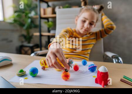 8 Jahre altes Mädchen spielt mit Planeten und Spielzeug Raumfahrer sitzen am Schreibtisch im Zimmer. Weibliche Grundschülerin macht ihre Hausaufgaben - Skulpturen Stockfoto