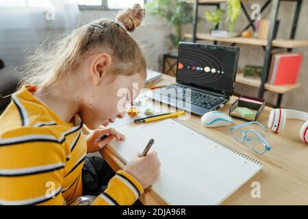 8 Jahre altes Mädchen studieren Sonnensystem sitzt am Schreibtisch im Zimmer. Grundschülerin macht ihre Hausaufgaben im Übungsbuch. Stockfoto