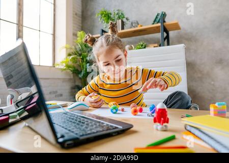 8 Jahre altes Mädchen mit Laptop, um online Planeten des Sonnensystems auf dem Schreibtisch im Zimmer sitzen zu studieren. Junge weibliche Grundschülerin beobachten Stockfoto