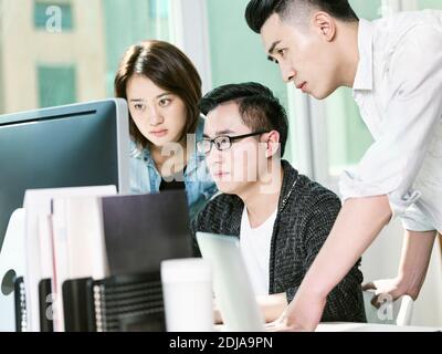 Team von drei Jungunternehmern, die Daten im Büro analysieren mit Desktop-Computer Stockfoto