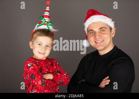 Schöner junger Vater posiert mit seinem Sohn, beide tragen Weihnachtskleidung vor grauem Hintergrund Stockfoto