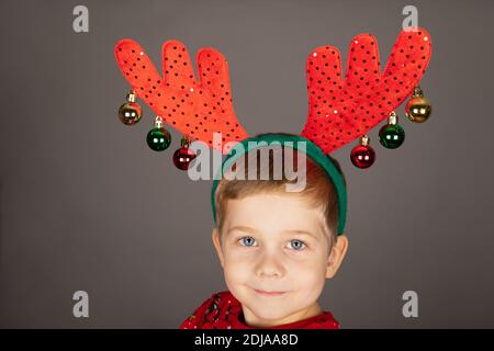 Niedlicher kleiner Junge mit Weihnachts-Outfit und Accessoires posiert in Vorderseite mit grauem Hintergrund Stockfoto