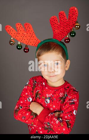 Niedlicher kleiner Junge mit Weihnachts-Outfit und Accessoires posiert in Vorderseite mit grauem Hintergrund Stockfoto