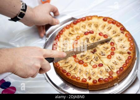 Mann schneidet hausgemachten Kuchen liegen auf runden Brett in Stücke mit Messer. Stockfoto