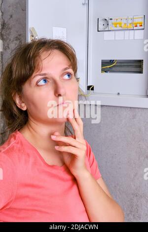 Verteilertafel im Haus und schalten Sie den Schalter aus. Eine junge Frau tief in Gedanken neben dem Sicherungskasten, kopieren Raum. Stromausfall in der Wohnung Stockfoto