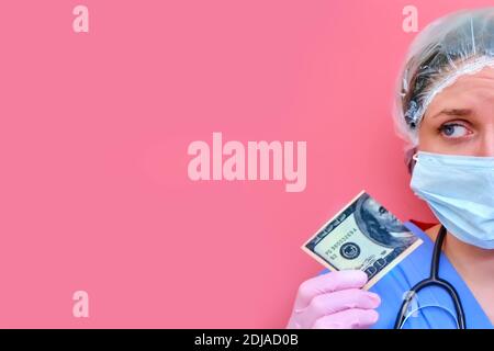 Eine Sanitäterin hält eine halbierte US-Dollar-Rechnung, Platz für Text kopieren. Eine Krankenschwester mit Geld für die Arbeit auf einem rosa Hintergrund, das Konzept der zahlenden Ärzte Stockfoto