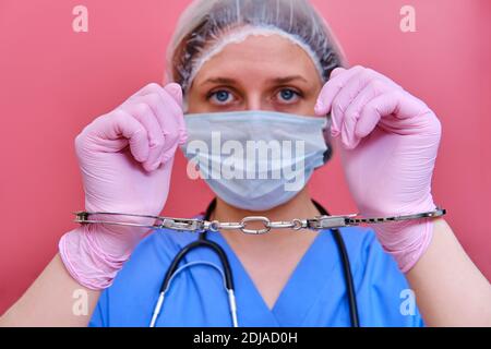 Doktor Hände in Handschellen auf rosa Hintergrund, Nahaufnahme. Junge Frau Hände in medizinischen Handschuhen mit Handschellen, Coronavirus Quarantäne-Konzept. Stockfoto