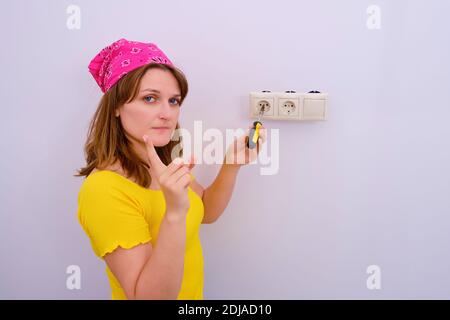 Die Frau schüttelt den Finger, um die Steckdose zu reparieren, den Raum zu kopieren. Warnung vor Sicherheitsvorkehrungen während der Reparatur. Stockfoto
