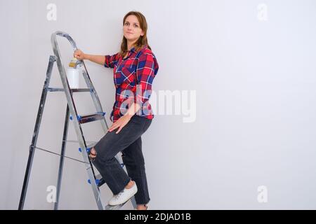 Malerin steht auf einer Trittleiter in einem karierten Hemd, Platz kopieren. Malen der Wände in einer neuen Wohnung Stockfoto