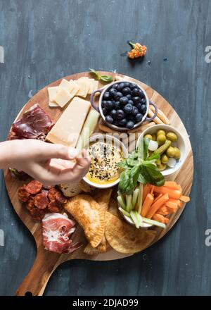 Blick von oben auf ein Holzschneidebrett voller leckerer spanischer Speisen. Eine Mädchenhand, die ein Essensstück hält, ist im Vordergrund unfokussiert. Stockfoto