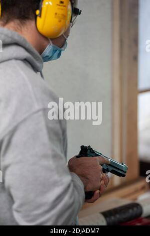 Mann im Schießstand, mit Kopfhörer zur Geräuschreduzierung, automatische Pistole in der Hand, bereit zum Schießen. Stockfoto