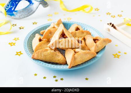 Jüdische Purim Hamantaschen hausgemachte Kekse oder Kekse auf dem Teller. Purim-Feiertagskonzept (jüdischer Faschingsurlaub) mit Keksen, Maske und gragger an Stockfoto