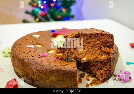 Nahaufnahme eines geschnittenen Plumenkuchen für Weihnachtsfeiern. Kuchen ist dekoriert und ein Weihnachtsbaum im Hintergrund. Stockfoto