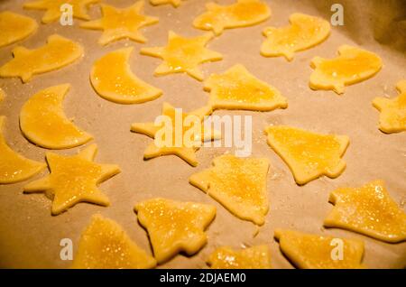 Hausgemachte goldene Plätzchen in Formen für weihnachten, Weihnachtsferien, auf braunem Backpapier auf einem Blech, Vorbereitung, vor dem Backen, süßen Zucker Dessert Stockfoto