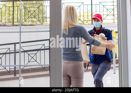 Kurier mit Thermorucksack, der einer jungen Geschäftsfrau frisches Mittagessen liefert. Konzept für die Lieferung von Speisen zum Mitnehmen Stockfoto