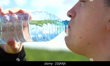 Durstlöschen. Trinken Sie sauberes Wasser aus einer Flasche. Ein junger Mann mit kaukasischem Aussehen trinkt Wasser aus einer transparenten Plastikflasche gegen ein Blau Stockfoto