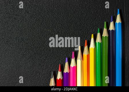 Satz Buntstifte auf schwarzem Hintergrund. Buntstifte auf einem Kreidetafel. Schwarze Textur mit Buntstiften. Harte Textur Stockfoto