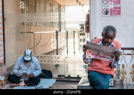 Jamnagar, Gujarat, Indien - Dezember 2018: Ein älterer indischer Mann, der eine Zeitung liest, die auf dem Bürgersteig sitzt. Stockfoto