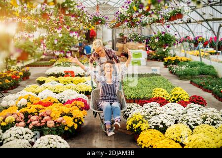 Zwei ziemlich verspielte Floristen Frauen mit einer lustigen Fahrt mit Wagen für eine Pause im Gewächshaus. Stockfoto