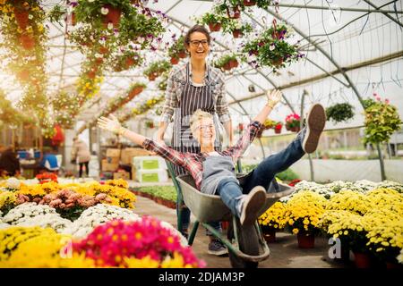 Zwei entzückende freudige Floristen Frauen Spaß mit Wagen für eine Pause im Gewächshaus. Stockfoto