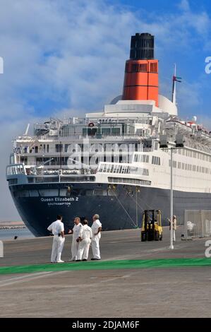 Gruppe von Offizieren und Crew aus dem abgeschossenen Costa Kreuzfahrtschiff Port Rashid Kulisse von Queen Elizabeth 2 QE2 QEII ex Cunard Liner wartet auf Umbau als Hotel Stockfoto