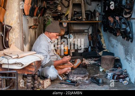 Jamnagar, Gujarat, Indien - Dezember 2018: Ein indischer Schuster, der in seinem Straßenladen an der Schuhreparatur arbeitet. Stockfoto