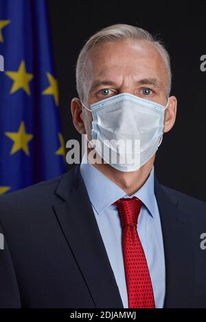 Vertikale Porträt von reifen Geschäftsmann oder Politiker tragen Maske und Blick auf die Kamera, während Sie im Hintergrund gegen die EU-Flagge stehen Stockfoto