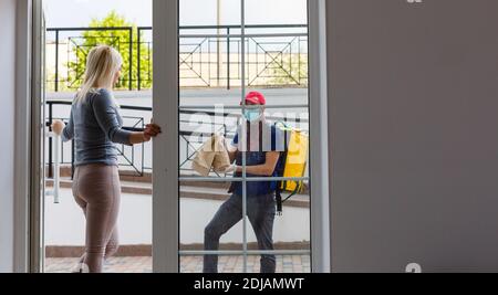 Kurier mit Thermorucksack, der einer jungen Geschäftsfrau frisches Mittagessen liefert. Konzept für die Lieferung von Speisen zum Mitnehmen Stockfoto
