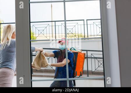 Kurier mit Thermorucksack, der einer jungen Geschäftsfrau frisches Mittagessen liefert. Konzept für die Lieferung von Speisen zum Mitnehmen Stockfoto