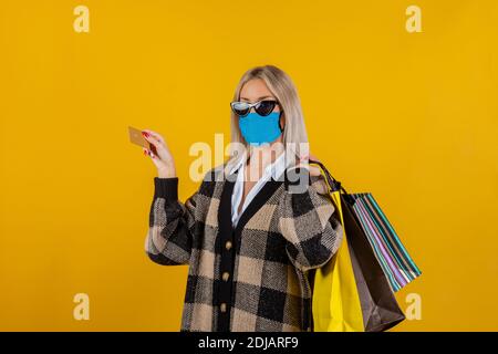 Modische Frau trägt eine grüne Sicherheits-Gaze-Maske zur Prävention von Coronavirus Covid19 Pandemie, mit Einkaufstaschen und Kreditkarte in der Hand Stockfoto