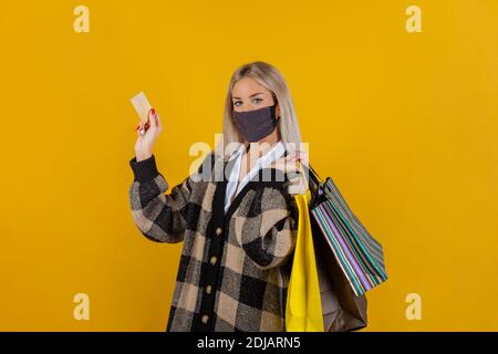 Modische Frau trägt eine grüne Sicherheits-Gaze-Maske zur Prävention von Coronavirus Covid19 Pandemie, mit Einkaufstaschen und Kreditkarte in der Hand Stockfoto