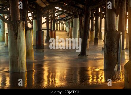 Unter Cocoa Beach Pier Florida USA bei Sonnenuntergang mit Silky Wasser Und Goldener Sonnenschein Spiegeln Sich Auf Dem Wasser Stockfoto