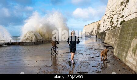 Brighton UK 14. Dezember 2020 - EIN Läufer und Radfahrer beobachten und ausweichen die Wellen in einem windigen Tag auf Saltdean undercliff Spaziergang an der Küste in der Nähe von Brighton bei Flut . Die Wettervorhersage ist für stärkere Winde und Duschen, um über Teile von Großbritannien zu verbreiten, aber mit Temperaturen, die wärmer als in den letzten Tagen sind : Credit Simon Dack / Alamy Live News Stockfoto