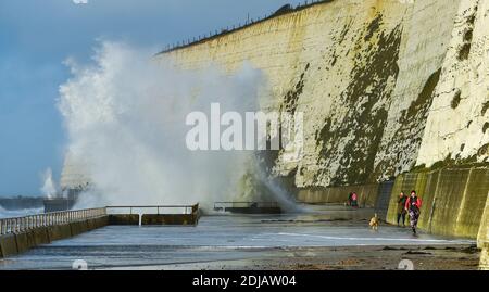 Brighton UK 14. Dezember 2020 - Wanderer und Läufer weichen den Wellen aus, die heute bei Flut bei Saltdean undercliff Walk in der Nähe von Brighton einstürzen. Die Wettervorhersage ist für stärkere Winde und Duschen, um über Teile von Großbritannien zu verbreiten, aber mit Temperaturen, die wärmer als in den letzten Tagen sind : Credit Simon Dack / Alamy Live News Stockfoto