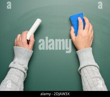 Hand hält ein Stück weiße Kreide auf dem Hintergrund eines leeren grünen Kreidetafel, zurück zur Schule Stockfoto