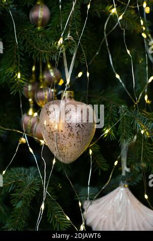Nahaufnahme Weihnachten und Neujahr Baumschmuck mit golden Leuchtendes Spielzeug in Herzform zwischen grünen Ästen und Girlande Leuchtet Stockfoto