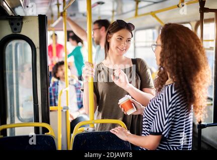 Zwei hübsche junge Frauen trinken Kaffee und unterhalten sich im Bus. Stockfoto