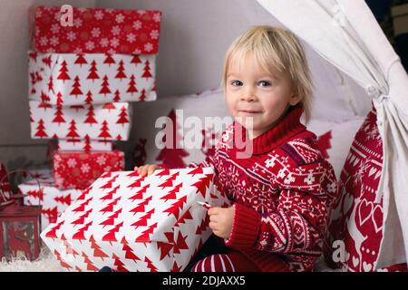 Niedliche kleine blonde Junge mit Weihnachts-Pullover, Eröffnung Geschenke zu Hause an Weihnachten Stockfoto