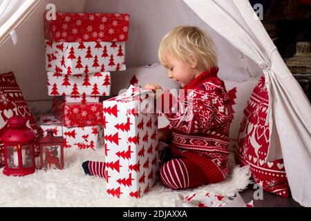 Niedliche kleine blonde Junge mit Weihnachts-Pullover, Eröffnung Geschenke zu Hause an Weihnachten Stockfoto